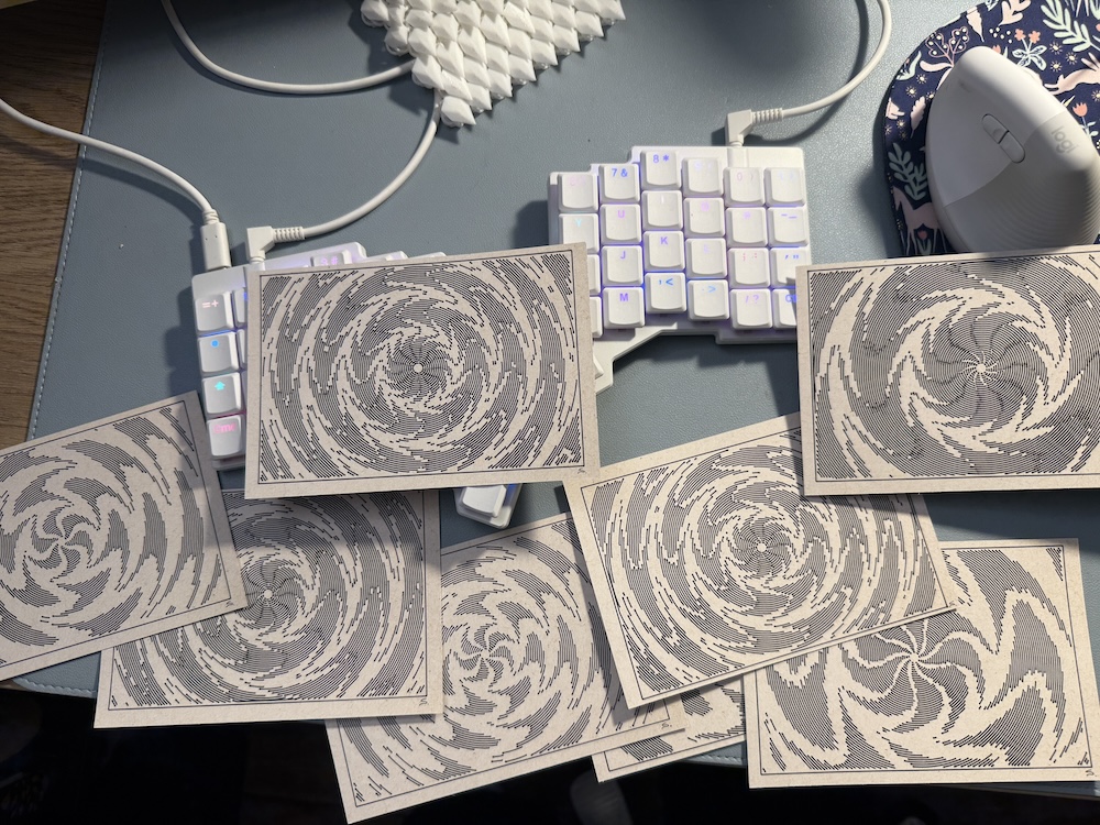 Pen-plotted mandala postcards with black ink ontop of a desk partially covering a keyboard.